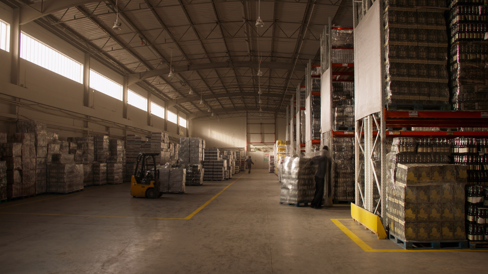 Modern beverage distribution warehouse interior with pallets of beer and wine cases on industrial racking — illustrating the operational scale of beverage distribution software